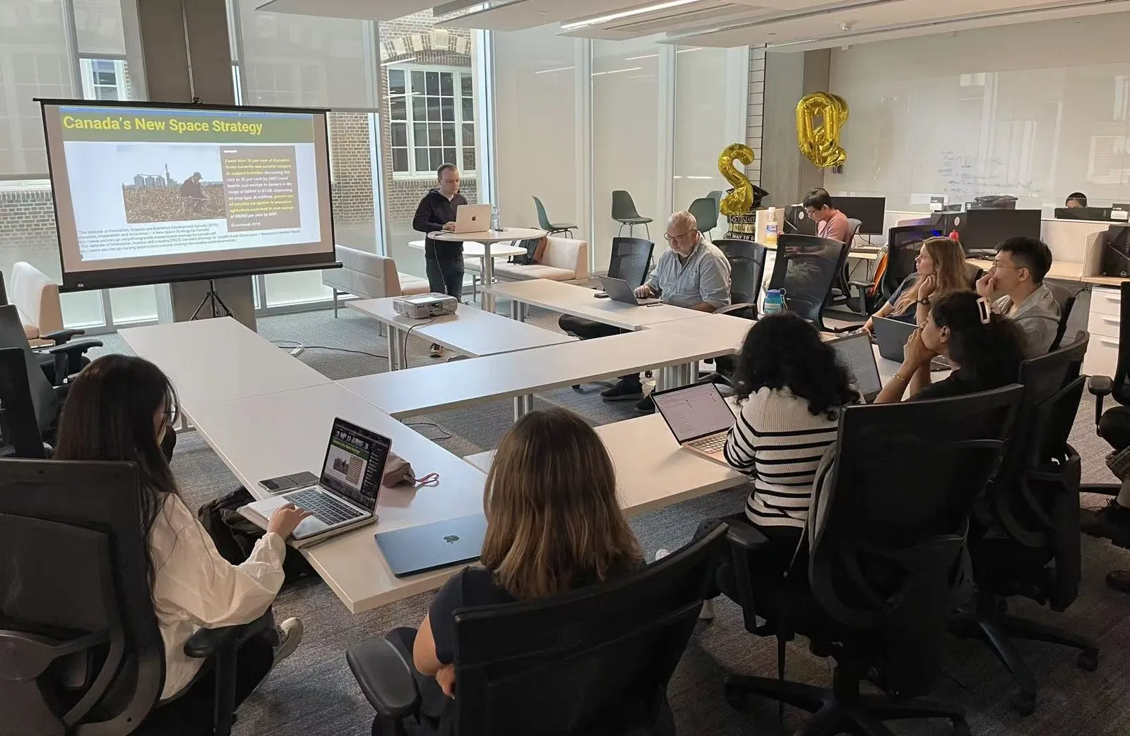 Joshua Billson presenting to the room and the Zoom audience